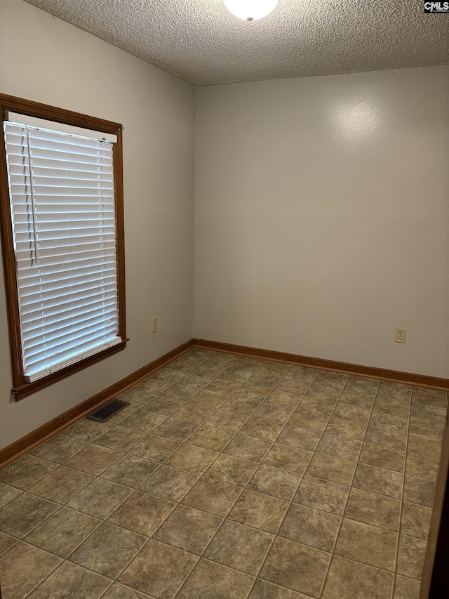 unfurnished room featuring baseboards, visible vents, and a textured ceiling