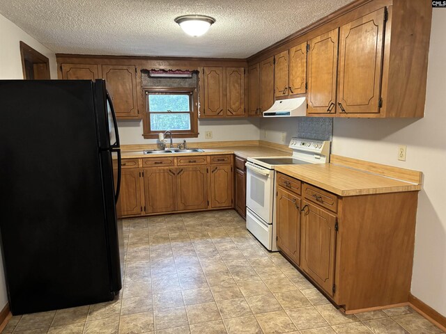 kitchen with under cabinet range hood, a sink, freestanding refrigerator, brown cabinetry, and electric range