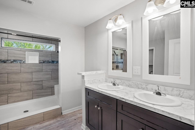 bathroom with baseboards, double vanity, a sink, and a tile shower
