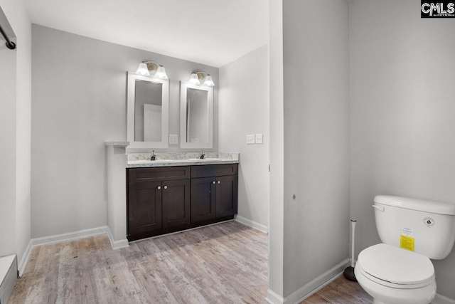 bathroom with baseboards, wood finished floors, toilet, and a sink