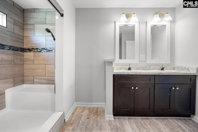 bathroom with baseboards, wood finished floors, double vanity, and a sink