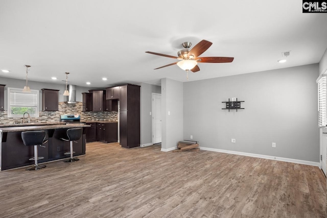 kitchen featuring a ceiling fan, dark brown cabinetry, a breakfast bar area, wall chimney range hood, and electric range