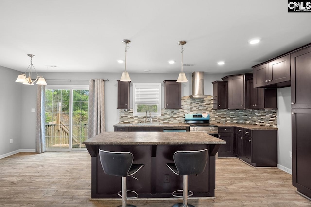 kitchen with light wood-style flooring, dark brown cabinets, stainless steel range with electric cooktop, a kitchen island, and wall chimney range hood