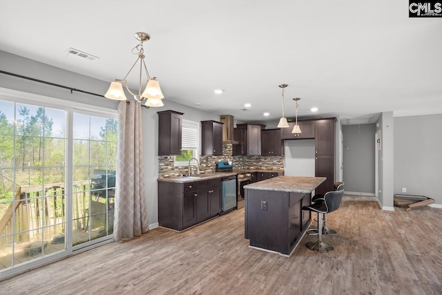 kitchen with dark brown cabinetry, a kitchen island, light wood finished floors, tasteful backsplash, and stainless steel dishwasher