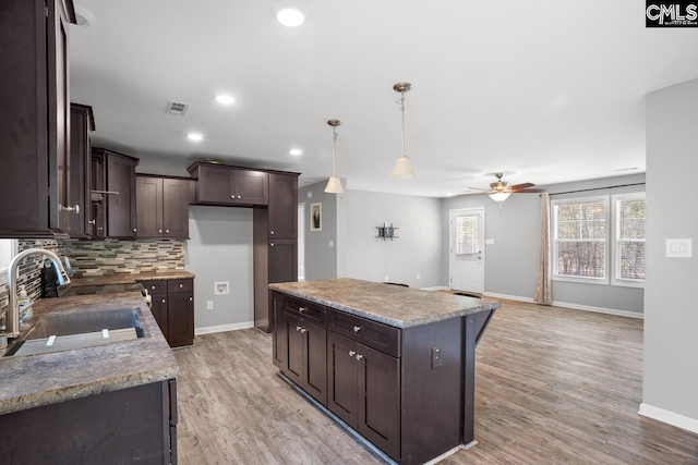 kitchen featuring visible vents, ceiling fan, dark brown cabinets, a kitchen island, and a sink