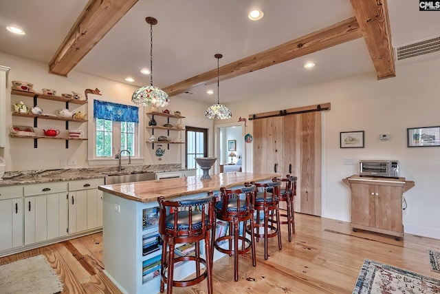 kitchen featuring a sink, open shelves, a breakfast bar area, a barn door, and a center island