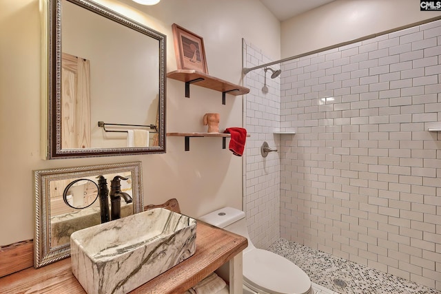 bathroom with a sink, toilet, tiled shower, and wood finished floors
