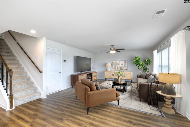 living area featuring baseboards, wood finished floors, ceiling fan, and stairway