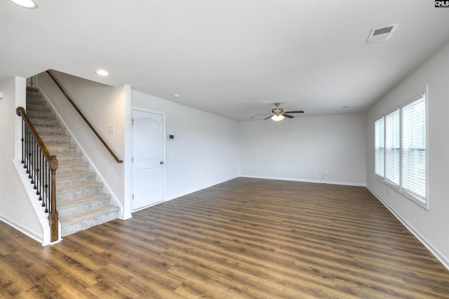 unfurnished living room featuring stairs, baseboards, visible vents, ceiling fan, and dark wood-type flooring