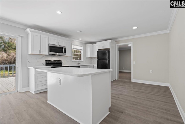 kitchen with light wood-type flooring, black appliances, light countertops, and tasteful backsplash