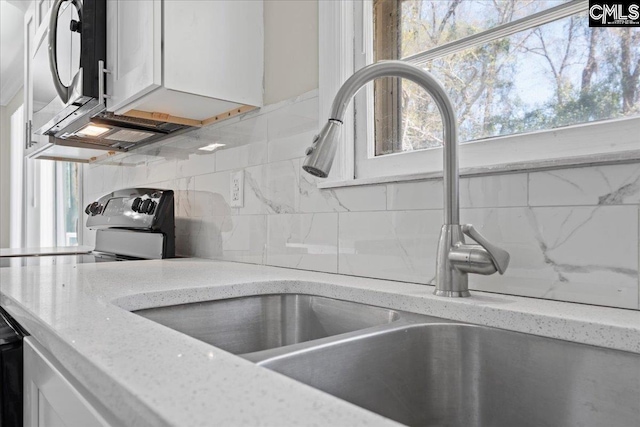 interior details featuring white cabinetry, tasteful backsplash, a sink, and range with electric cooktop