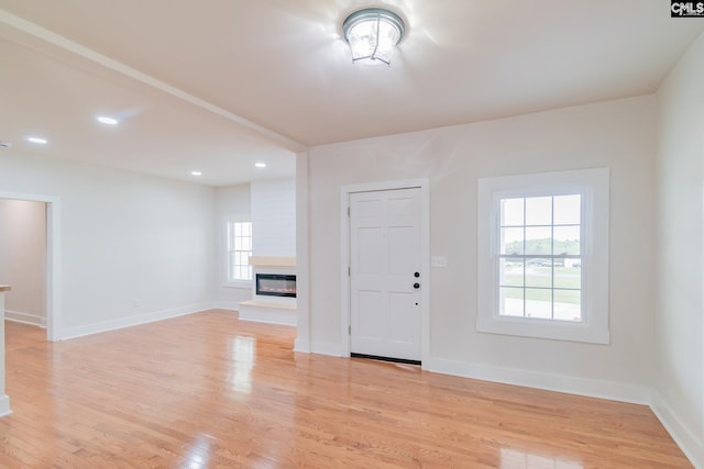 foyer featuring light wood finished floors, baseboards, recessed lighting, and a glass covered fireplace