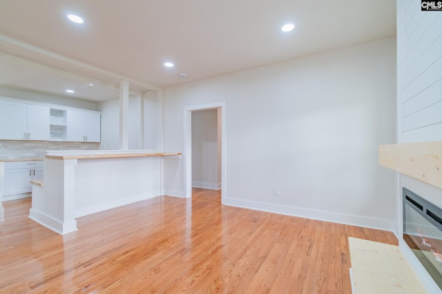unfurnished living room featuring baseboards, a glass covered fireplace, recessed lighting, and light wood finished floors