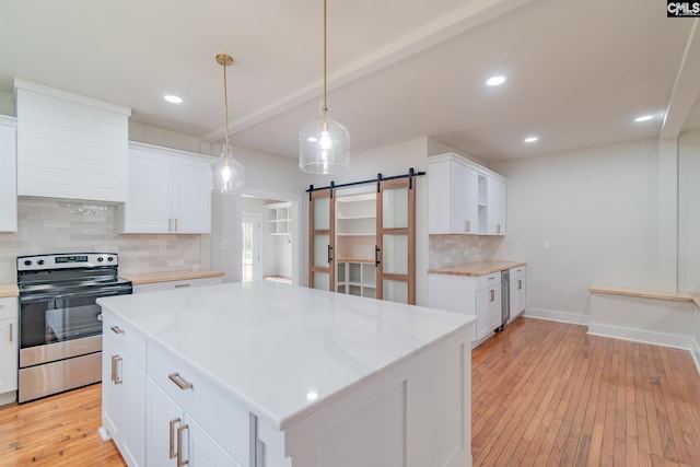 kitchen with light wood finished floors, stainless steel appliances, a barn door, white cabinetry, and backsplash