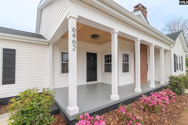 view of exterior entry with a chimney and covered porch