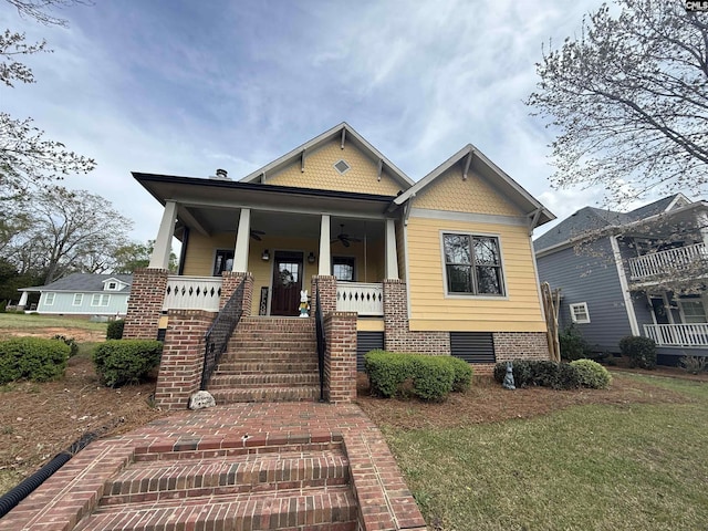 view of front of home with covered porch, ceiling fan, a front yard, and stairway