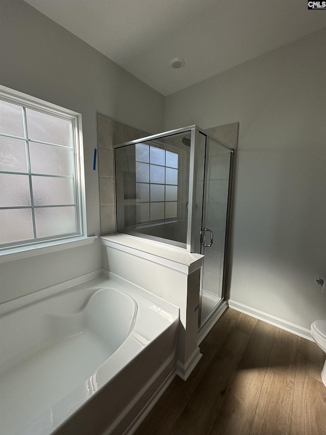 bathroom featuring wood finished floors, a garden tub, a stall shower, and baseboards