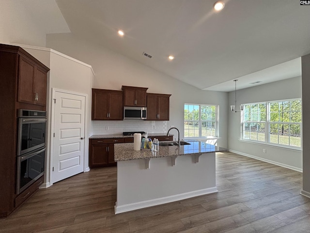 kitchen with light stone counters, a breakfast bar area, a sink, stainless steel appliances, and a kitchen island with sink