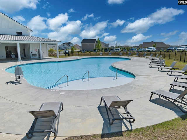 community pool with a patio, fence, and a residential view