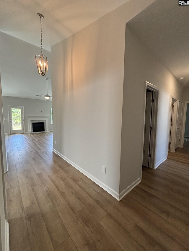 unfurnished living room featuring a fireplace, ceiling fan with notable chandelier, dark wood-style flooring, and baseboards