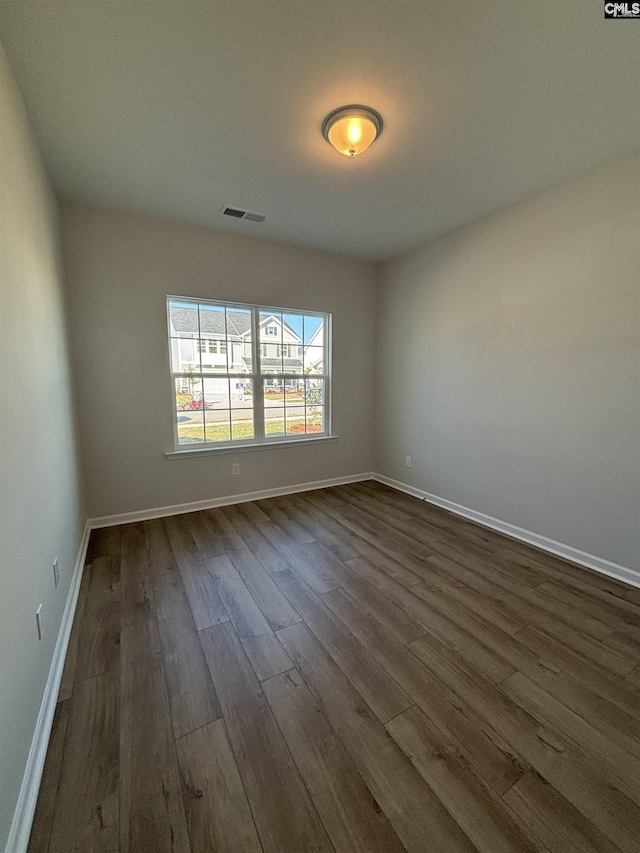 unfurnished room featuring dark wood-type flooring, visible vents, and baseboards