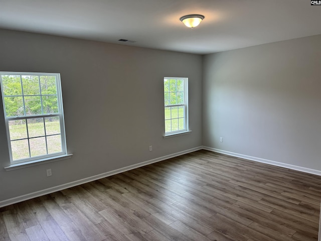 unfurnished room with dark wood finished floors, visible vents, a wealth of natural light, and baseboards