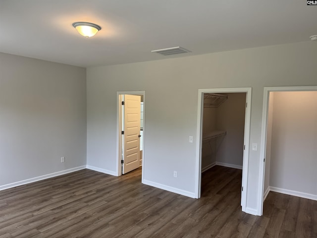unfurnished bedroom featuring dark wood-style flooring, visible vents, baseboards, and a walk in closet