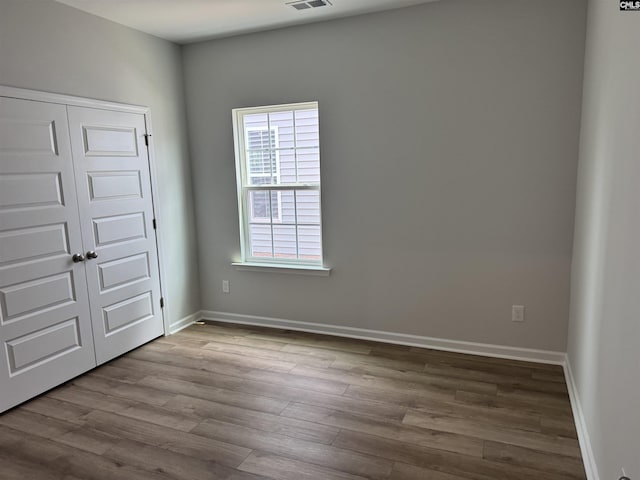 unfurnished bedroom featuring wood finished floors, a closet, visible vents, and baseboards