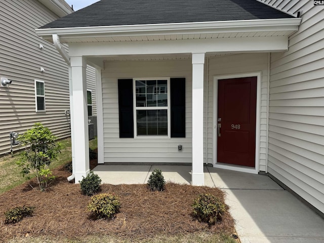 view of exterior entry with a shingled roof and covered porch