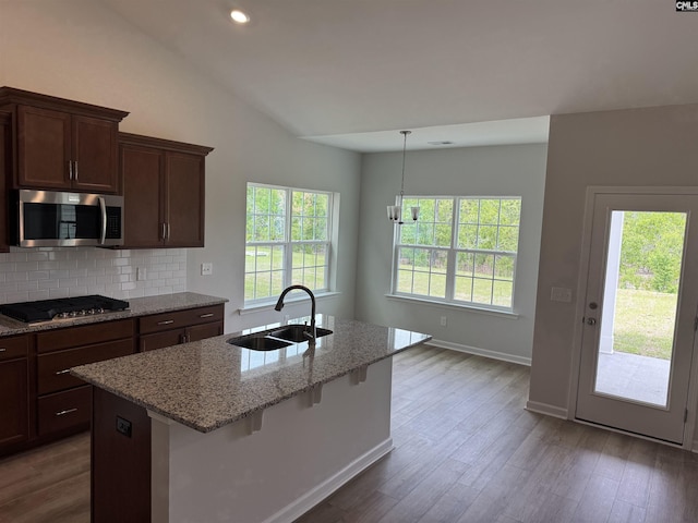 kitchen with tasteful backsplash, light stone counters, appliances with stainless steel finishes, a sink, and dark wood-type flooring