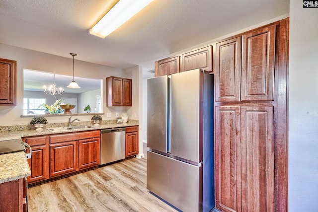 kitchen featuring light wood-style flooring, decorative light fixtures, brown cabinetry, stainless steel appliances, and a sink