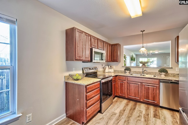 kitchen featuring light wood-style flooring, brown cabinetry, appliances with stainless steel finishes, a sink, and decorative light fixtures