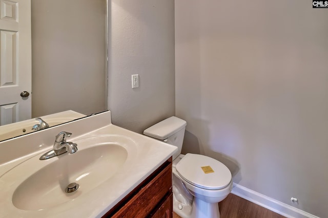 bathroom with toilet, wood finished floors, vanity, and baseboards