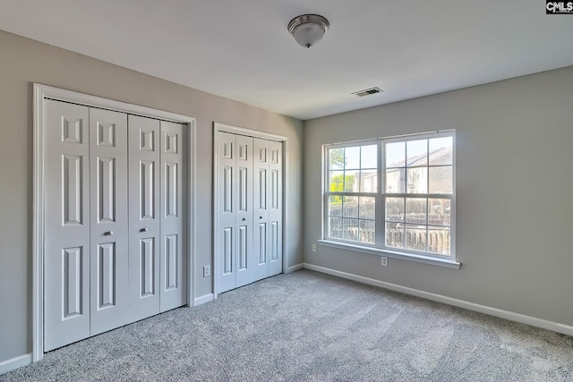 unfurnished bedroom with visible vents, carpet, two closets, and baseboards