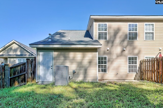 rear view of house with central AC, fence, and a yard
