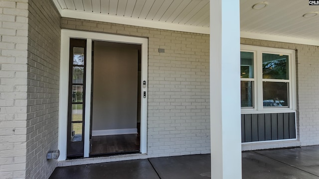 view of exterior entry with a porch and brick siding