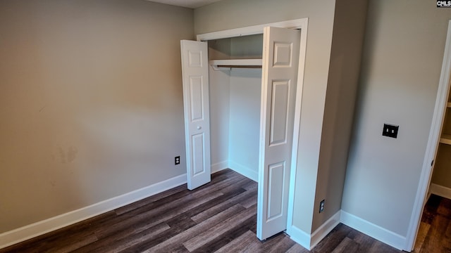 unfurnished bedroom featuring a closet, dark wood-type flooring, and baseboards