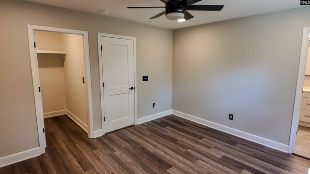unfurnished bedroom featuring a closet, baseboards, a walk in closet, connected bathroom, and dark wood-type flooring