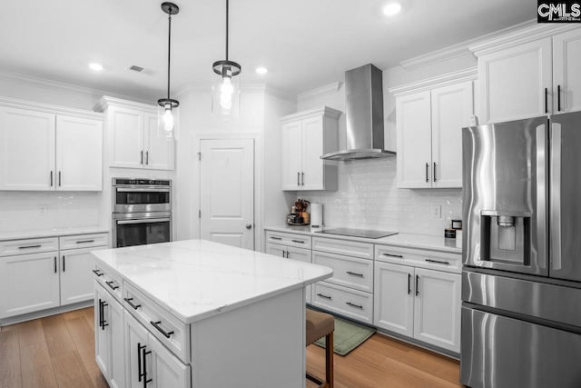 kitchen with stainless steel appliances, a kitchen island, wall chimney range hood, white cabinetry, and visible vents