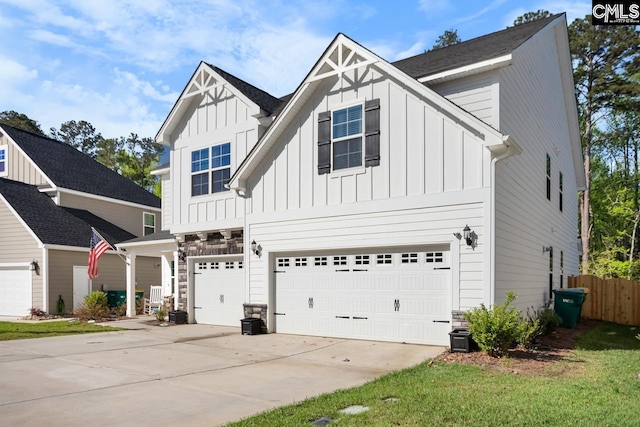 modern farmhouse with a garage, driveway, stone siding, board and batten siding, and fence