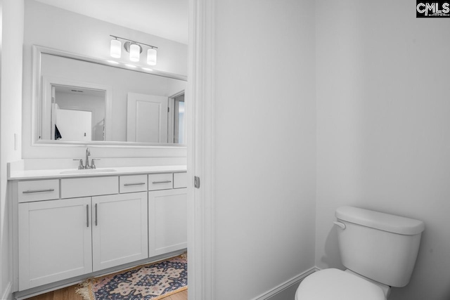 bathroom with wood finished floors, vanity, toilet, and baseboards