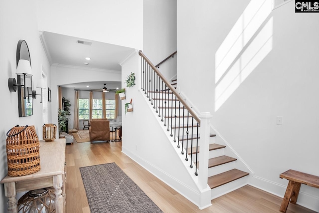 staircase featuring wood finished floors, ornamental molding, ceiling fan, baseboards, and visible vents