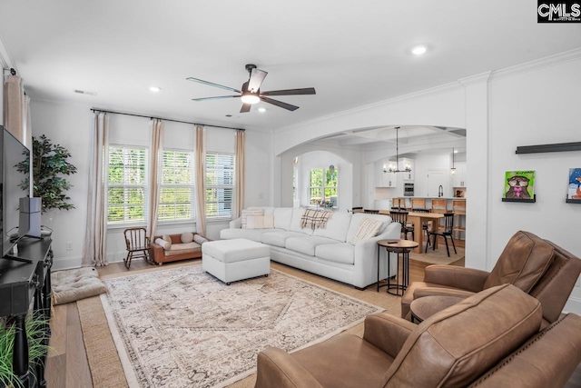 living area with a healthy amount of sunlight, light wood-style floors, ceiling fan with notable chandelier, and arched walkways
