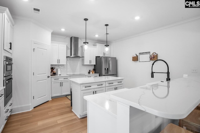kitchen with wall chimney range hood, appliances with stainless steel finishes, light wood-type flooring, ornamental molding, and a peninsula