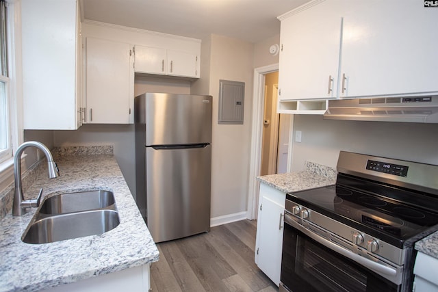 kitchen with electric panel, a sink, under cabinet range hood, wood finished floors, and stainless steel appliances
