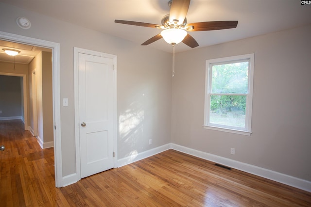 unfurnished room with a ceiling fan, visible vents, attic access, light wood finished floors, and baseboards