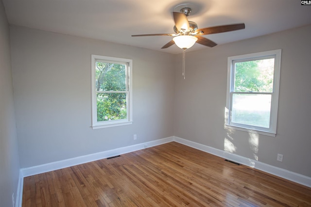 empty room with visible vents, a wealth of natural light, wood finished floors, and baseboards