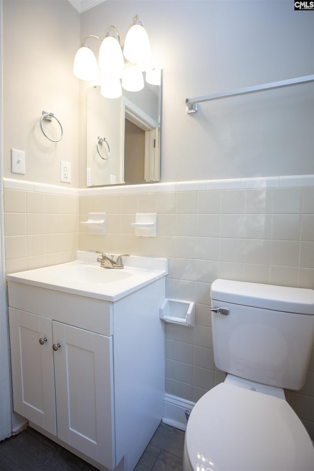 half bathroom featuring tile walls, toilet, vanity, a wainscoted wall, and tile patterned flooring