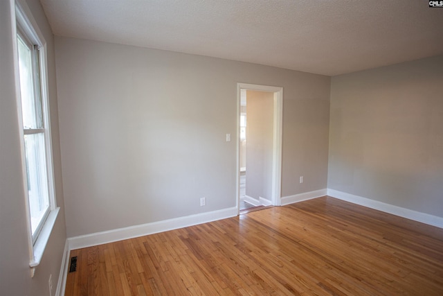 empty room featuring baseboards, light wood-type flooring, and a textured ceiling