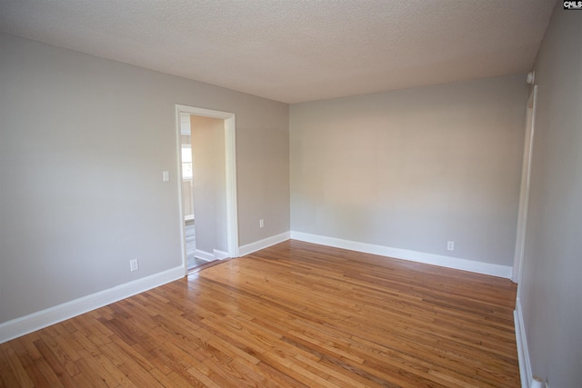 spare room with baseboards, light wood-type flooring, and a textured ceiling